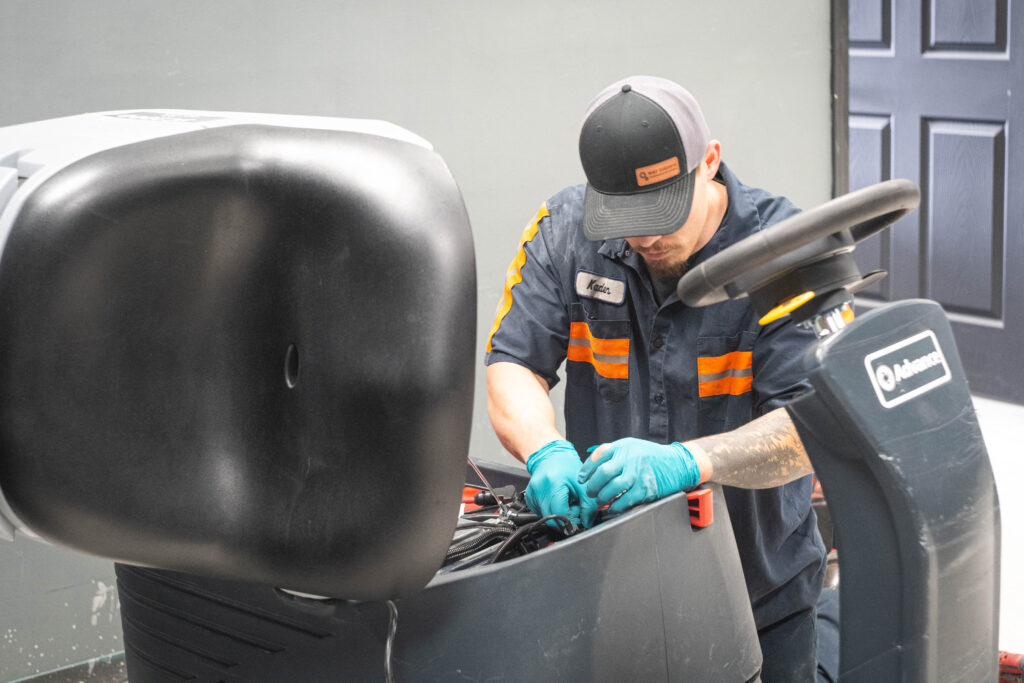 WaySolutions technician Kaden performs internal electrical wiring maintenance on an Advance ride-on floor scrubber.