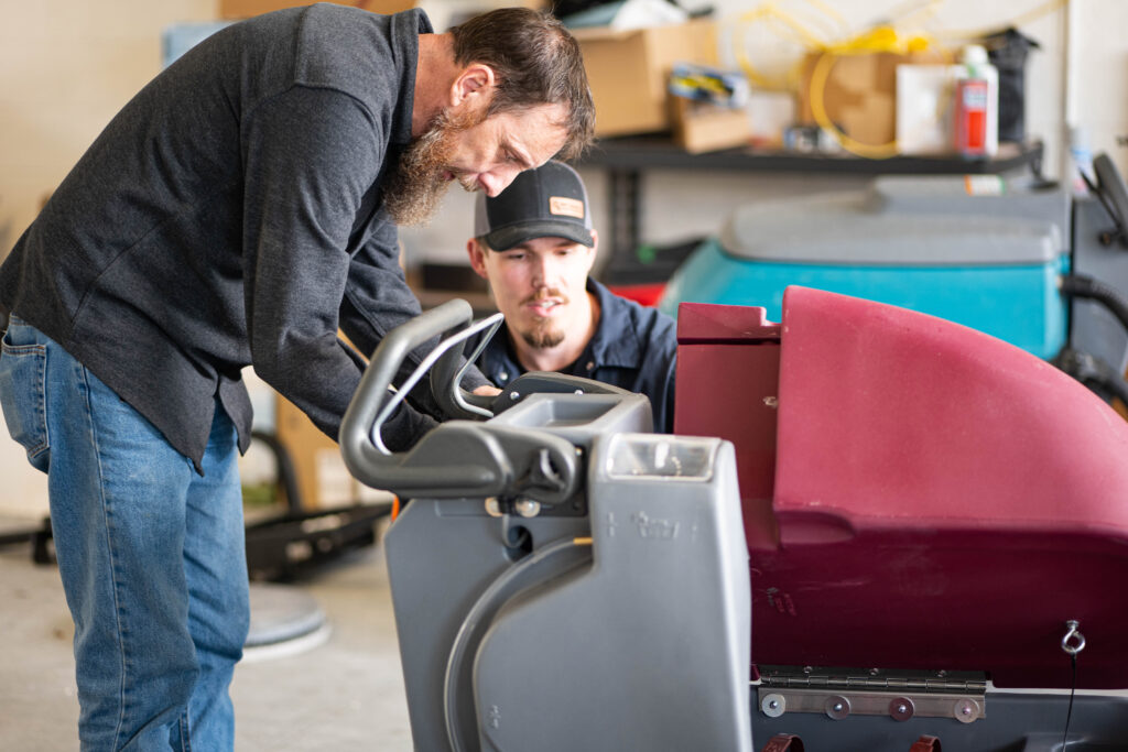 A WaySolutions technician and a facility manager inspect the control panel of a Minuteman E20 floor scrubber together.