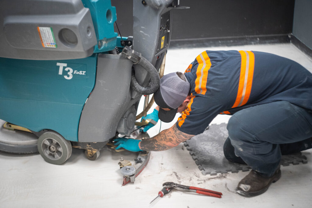 A WaySolutions technician uses hand tools to repair the lower squeegee assembly on a Tennant T3 floor scrubber in Layton, Utah.