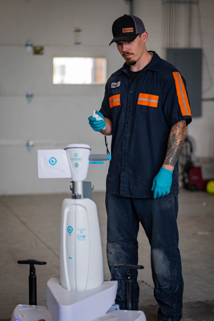 A white i-mop XL autonomous robotic floor scrubber stationed at the WaySolutions repair facility in Layton, Utah.

