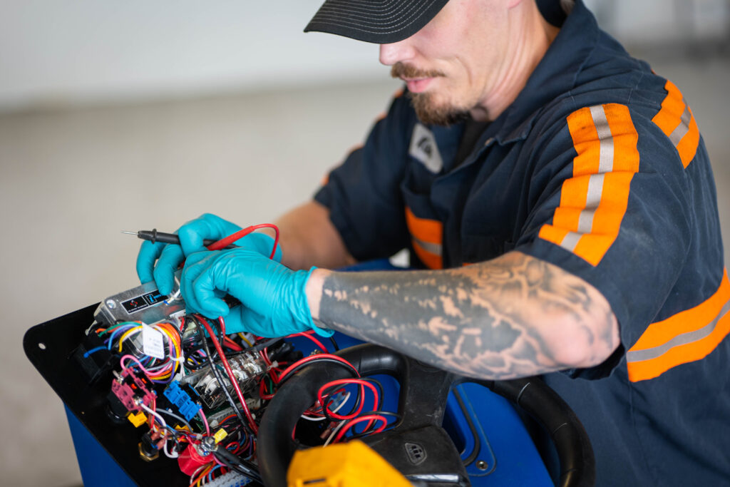 A WaySolutions technician uses a digital multimeter to test the complex circuit board of a commercial floor scrubber in Layton, Utah.